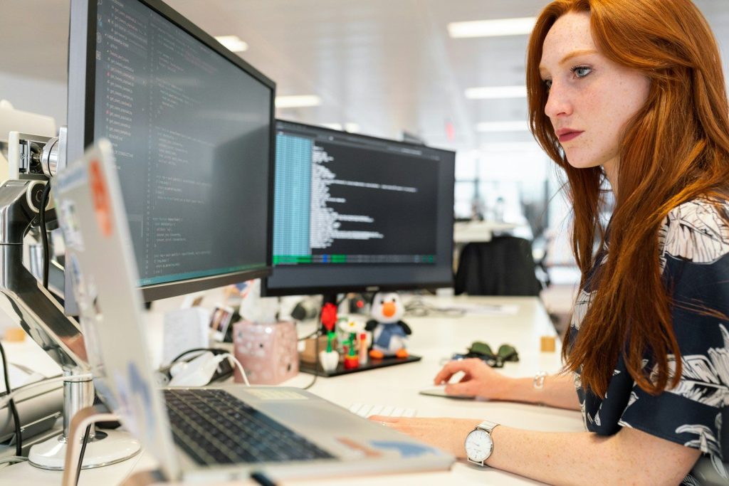 woman in green shirt sitting in front of computer; IT asset inventory tools